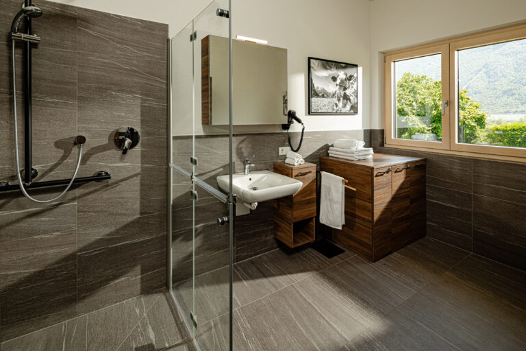 Badezimmer mit Dusche, Waschbecken und Fenster ins Grüne